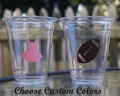 two shot glasses with football and dress silhouettes on them, sitting on a table