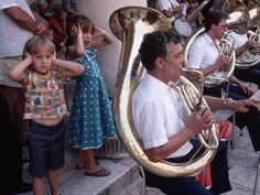 a group of people playing musical instruments in front of a building with children watching them