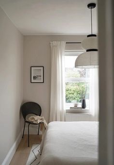 a bedroom with a bed, chair and window in the corner is seen from across the room