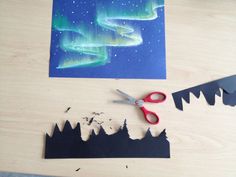 paper cut out to look like the northern lights with scissors next to it on a table