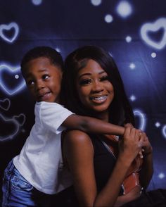 a woman holding a young boy in front of a wall with hearts on it and stars