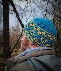 a bearded man wearing a blue and yellow knitted beanie hat in the woods