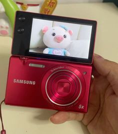 a person holding a red camera with a stuffed animal on it's display screen