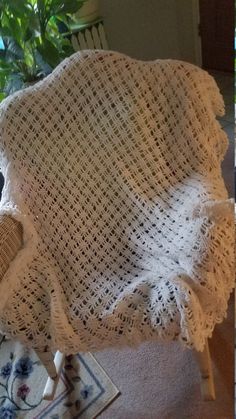 a chair covered in a white crochet blanket next to a potted plant