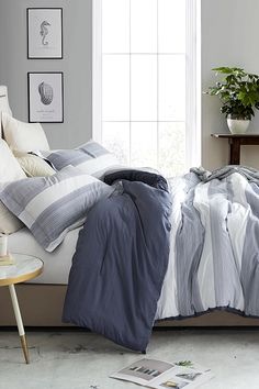 an unmade bed with blue and white striped comforter in front of a window