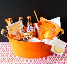 an orange bucket filled with lots of different types of drinks and snacks sitting on top of a table