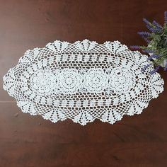 a white doily sitting on top of a wooden table next to a purple flower