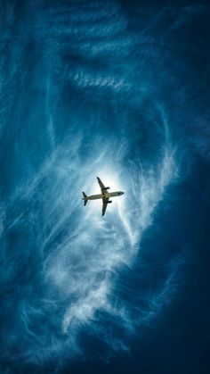 an airplane is flying through the blue sky with clouds in the foreground and sun behind it