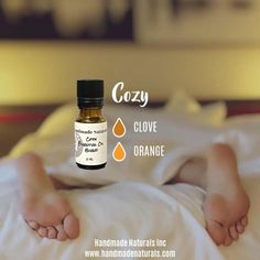 a bottle of orange essential oil sitting on top of a bed next to someone's feet