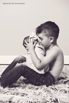 a young boy is sitting on the floor with his hands in his mouth while holding a stuffed animal