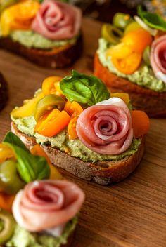 small sandwiches with vegetables and meats on them sitting on a wooden table, ready to be eaten