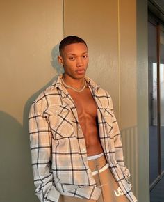 a shirtless man leaning against a wall with his hands in his pockets and looking at the camera