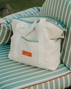 Elegant canvas tote bag with minimalist design and green detailing, resting on a striped outdoor cushion for a sophisticated coastal vibe