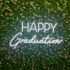 the words happy graduation are lit up in front of a green wall covered with flowers