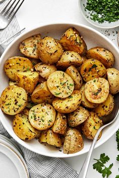 a white bowl filled with cooked potatoes and garnished with parsley on the side