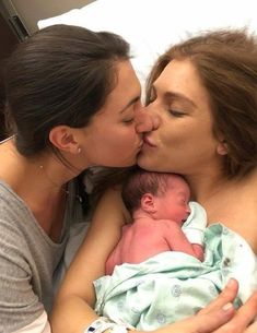 a woman kissing her baby while laying in bed with two other women and one man