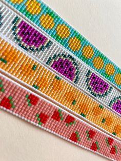 three strips of colorful beaded ribbon on a white surface with an orange, pink, yellow and green design