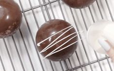 three chocolate donuts with white icing on a cooling rack next to a person's hand