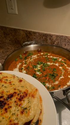 some food is sitting on a plate next to a skillet with sauce and bread