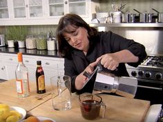 a woman pouring something into a glass on top of a wooden table in a kitchen