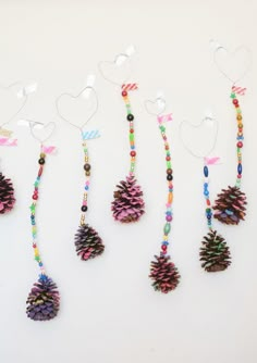 five pine cones are hanging from strings on a white surface, with hearts and ribbons attached to them