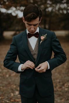 a man in a suit and bow tie is looking down at his pocket while wearing a boutonniere