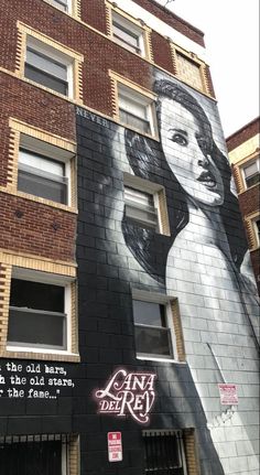 a large mural on the side of a building in an urban area, depicting a woman with long hair