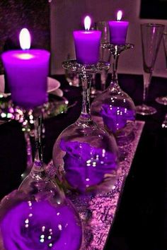 purple candles are sitting in glass vases on a table with plates and wine glasses