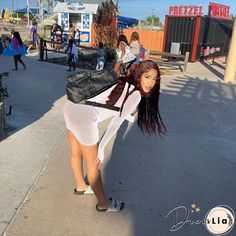 a woman with long hair is standing on the sidewalk and holding a black bag behind her back