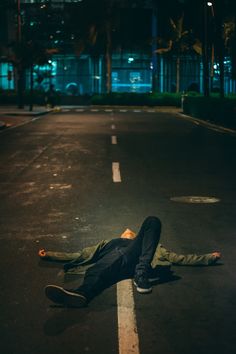 a man laying on the ground in an empty street at night with his head down