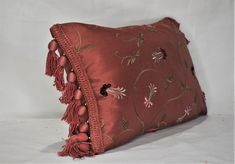 a red pillow with tassels and flowers on the front is sitting on a white surface