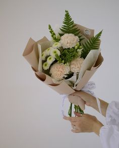 a bouquet of flowers is being held by a woman's hand in front of a white wall