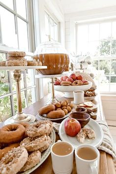 an assortment of donuts, apples, and coffee on a table in front of windows