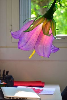 a purple flower hanging from a ceiling in front of a laptop computer on a desk