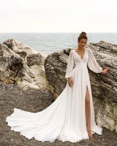 a woman in a long white dress standing on rocks near the ocean with her legs spread out