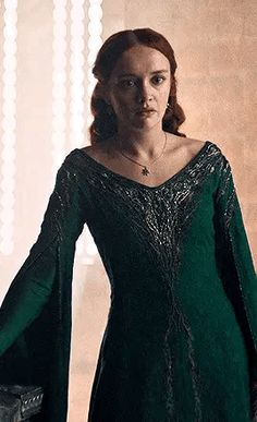 a woman in a green dress is standing with her hands on her hips and looking off to the side