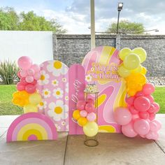 a pink and yellow birthday decoration with balloons