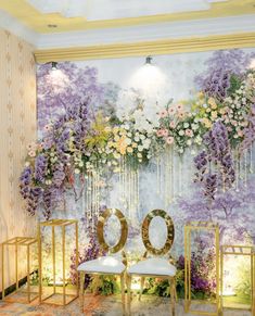 two white chairs sitting in front of a wall with purple flowers and greenery on it