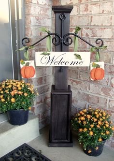 a welcome sign with pumpkins and flowers in front of a brick wall