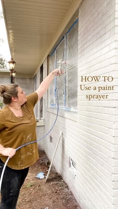 a woman painting the side of a house with spray paint and a hose attached to it