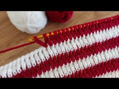 a red and white striped crochet blanket next to balls of yarn