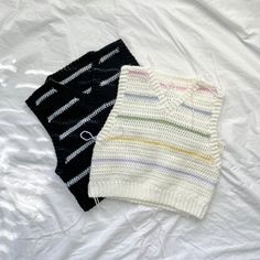 two knitted sweaters laying on top of a white sheet