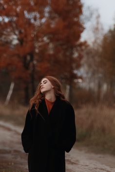 a woman standing in the middle of a dirt road with her eyes closed looking up