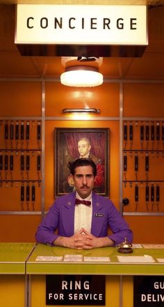 a man in a purple jacket and bow tie sitting at a counter