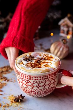 a woman is holding a cup of hot chocolate with cinnamon and star anise on top