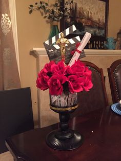 a wooden table topped with a vase filled with red flowers and movie claps on top of it