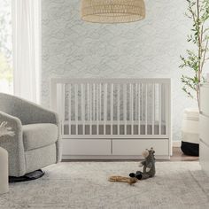 a baby crib with a teddy bear on the floor next to it and a lamp hanging above