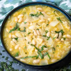 a bowl filled with white beans and greens on top of a blue cloth next to a spoon