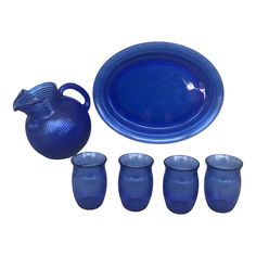 a blue pitcher and four glasses next to each other on a white surface with an empty plate in the middle