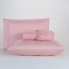 a bed with pink sheets and pillows on top of each other, in front of a white wall